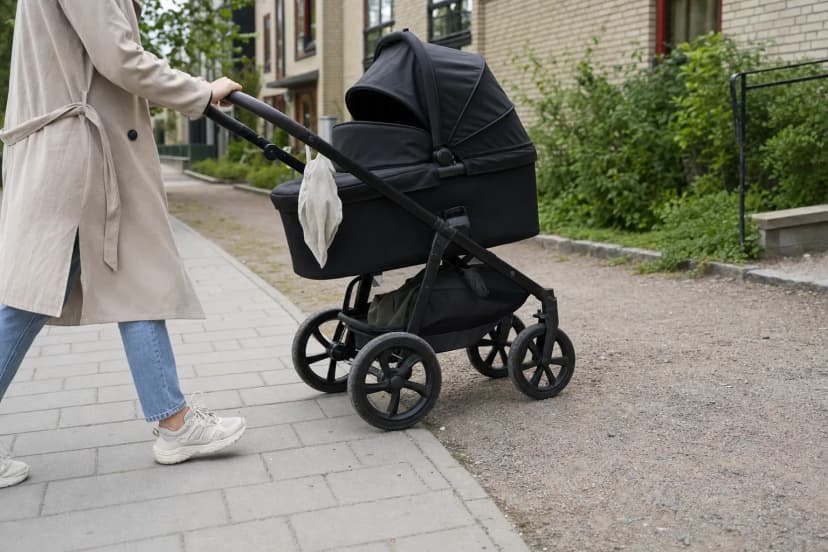Förälder kör en barnvagn från en trottoar över på en grusväg