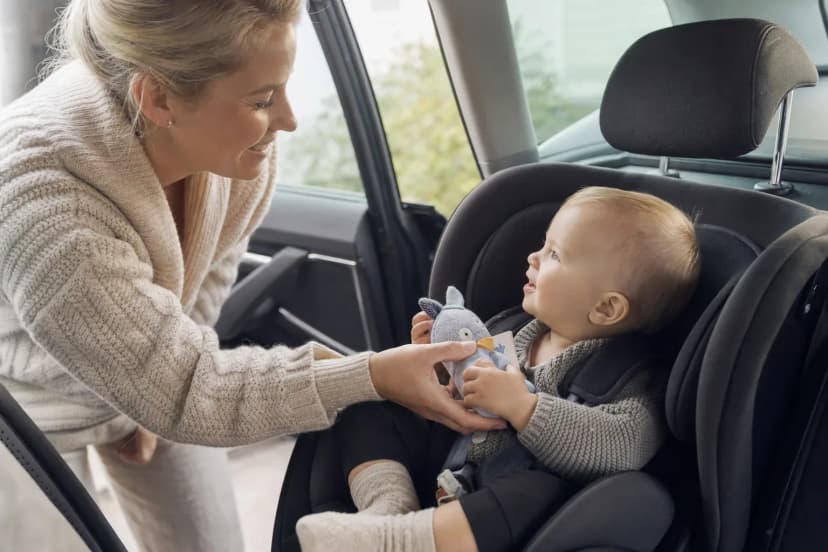 Förälder räcker en mjuk leksak till ett barn som sitter fastspänt i en bilbarnstol.