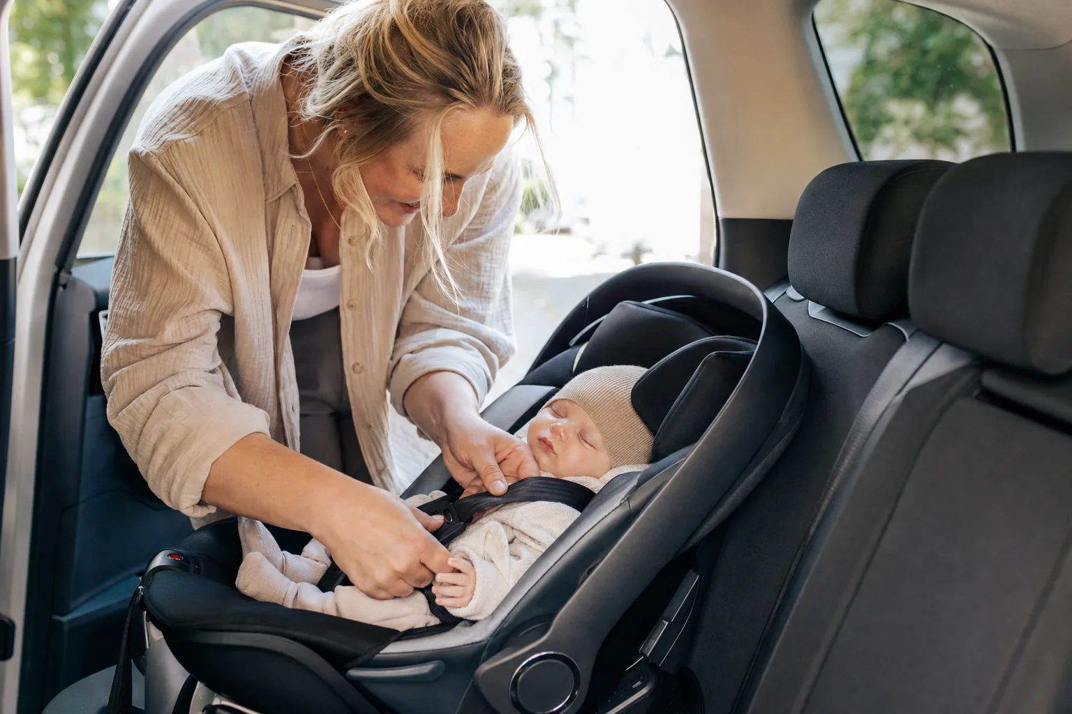 Förälder spänner fast en nyfödd bebis i ett babyskydd i bilens baksäte.
