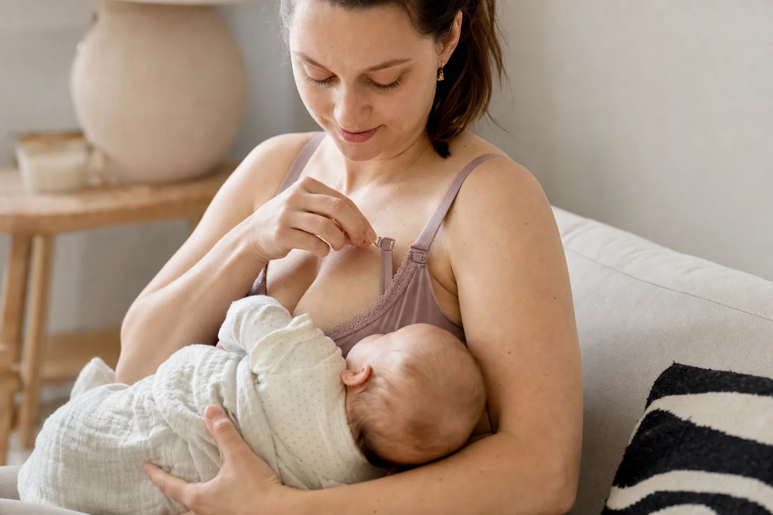 Nybliven mamma öppnar en amnings-bh med en hand medan hon håller sin bebis.